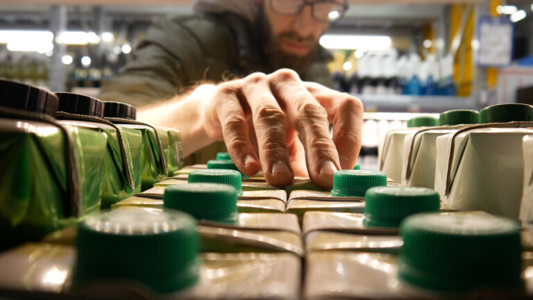 close up of carton packaging of wine on a store shelf and a man takes one